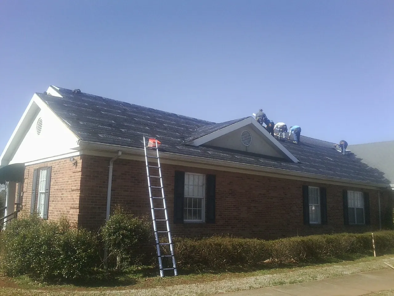 Crew tearing shingles off a brick ranch roof with a ladder set — Metal Roof Repair work by our crew in Greenbrier