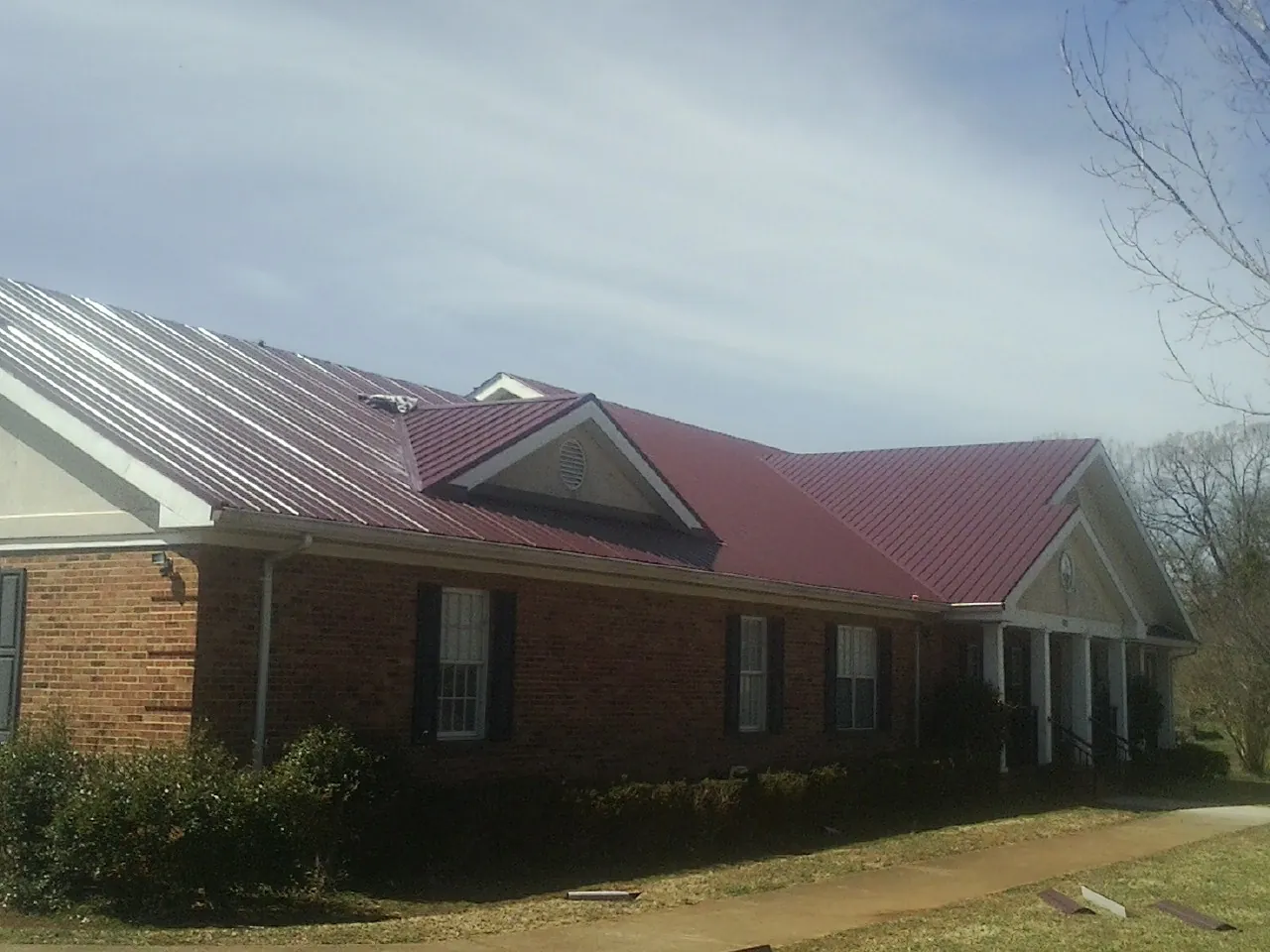 Red metal roof with gabled entries on a long brick building, from a Hail Damage Roof Repair job in Greenbrier