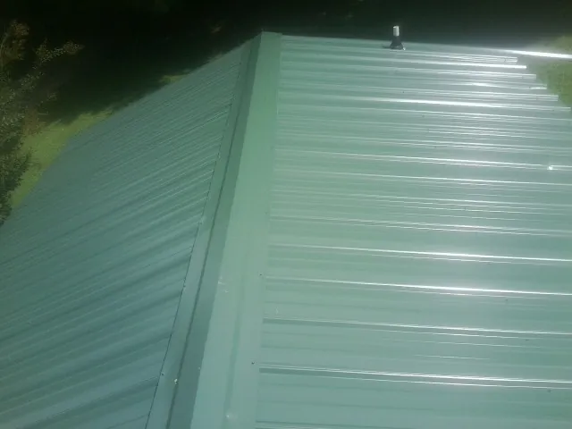 New green metal panels meeting at the ridge of a roof — Flat Roof Repair work by our crew in Greenbrier