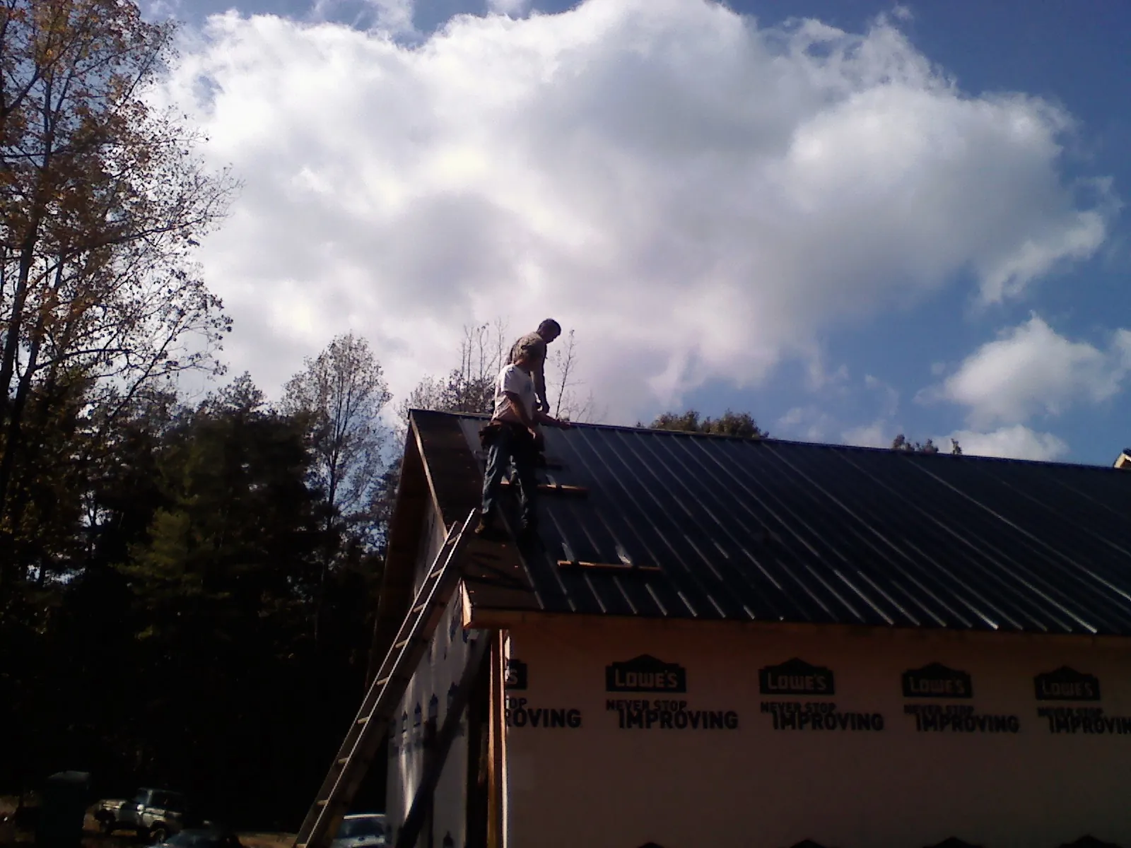 Roofer fastening dark metal panels high against a cloudy sky, from a Roof Inspection job in Greenbrier