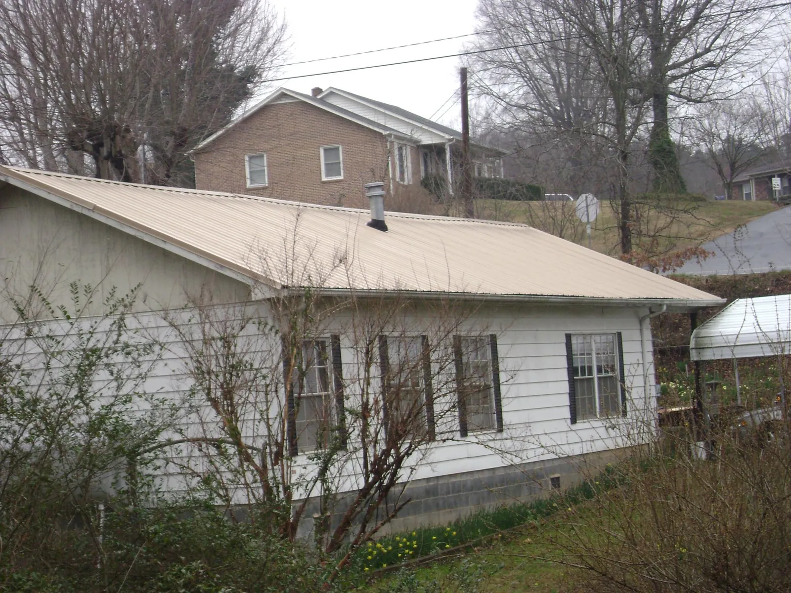 Tan metal roof on a white sided house set into a hillside — Commercial Roofing by Roofing Brothers in Greenbrier