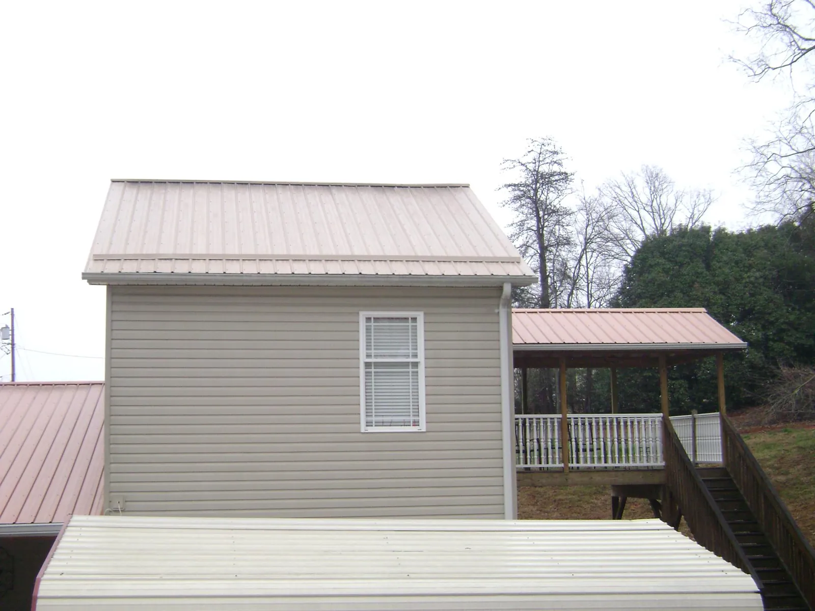 Tan metal roofs on a two story addition and attached porch, from a Roof Replacement job in Greenbrier